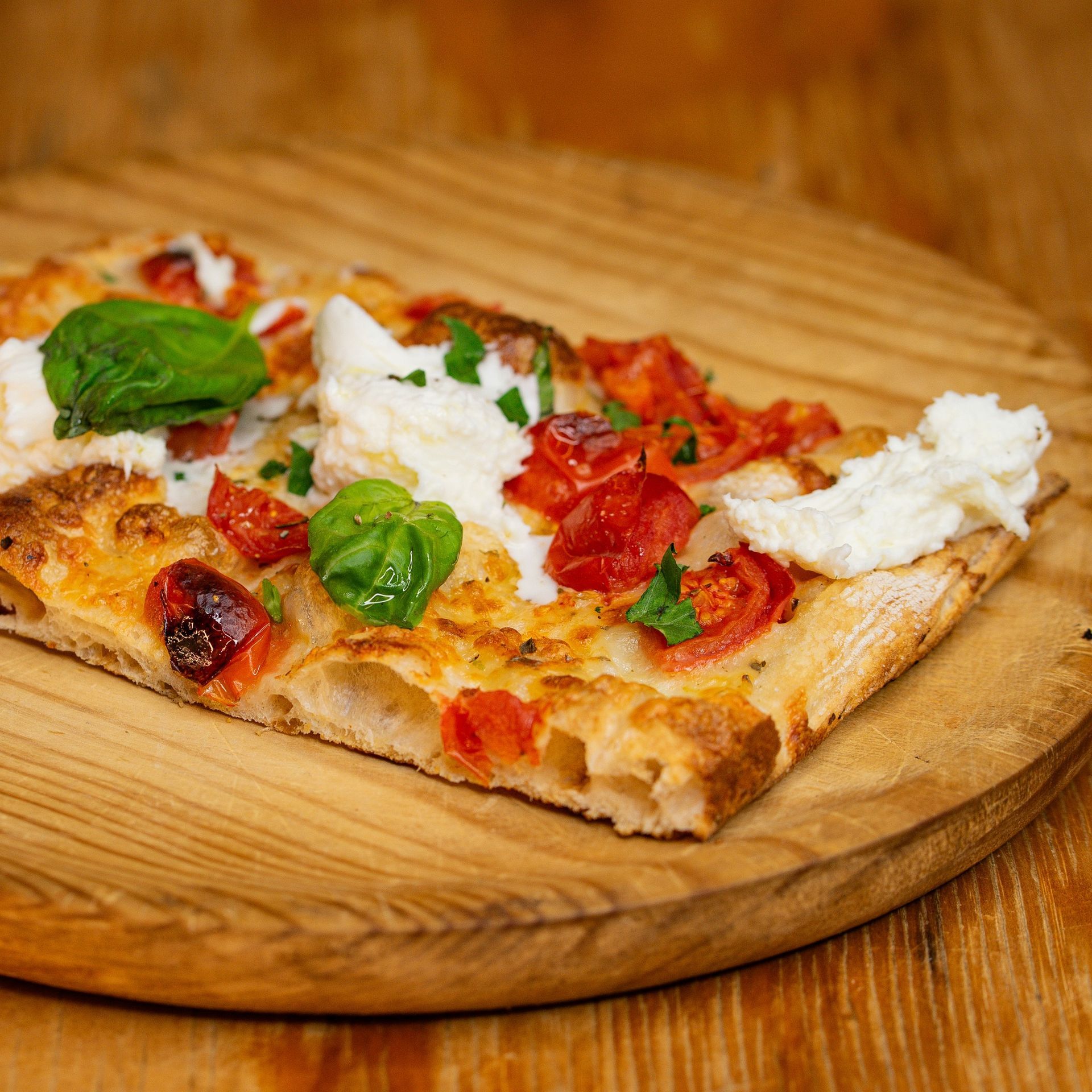 Una fetta di pizza con pomodori e basilico su un tagliere di legno.