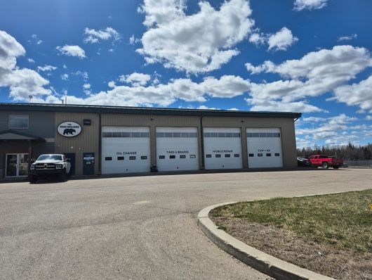 Industrial building with four garage doors, parked vehicles, and a cloudy blue sky