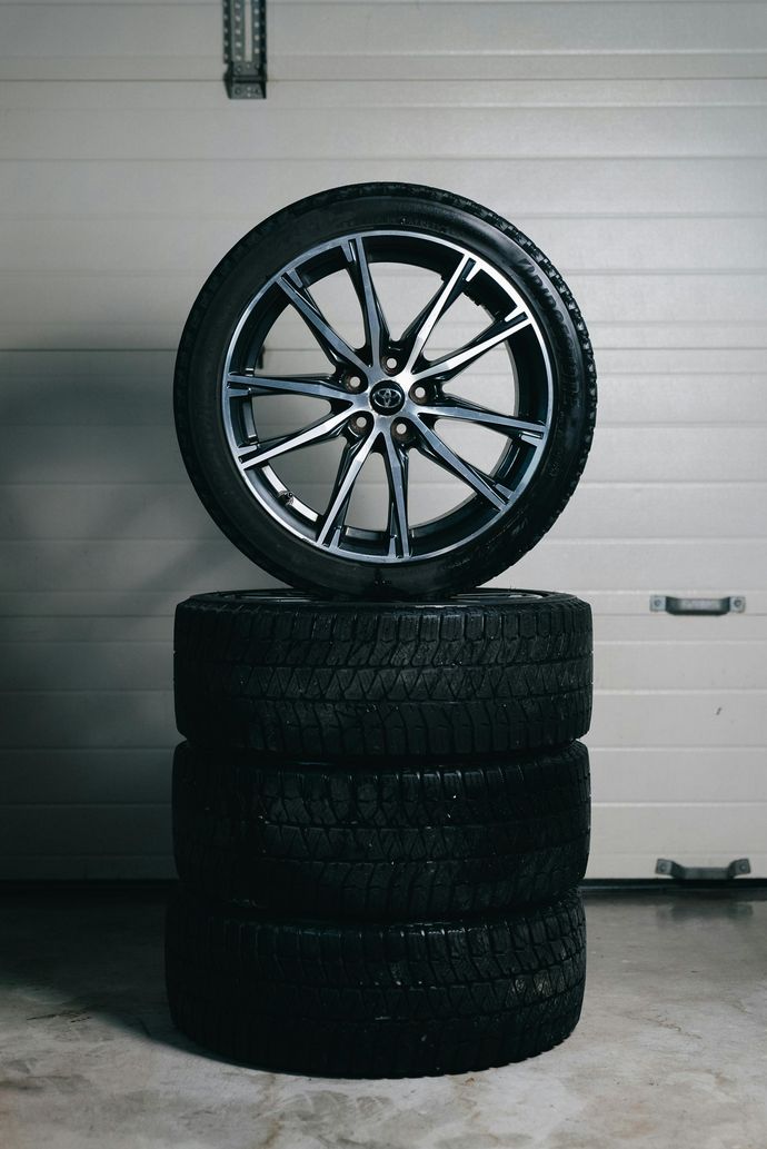 Car wheel rim balanced on a stack of four black tires in a garage.