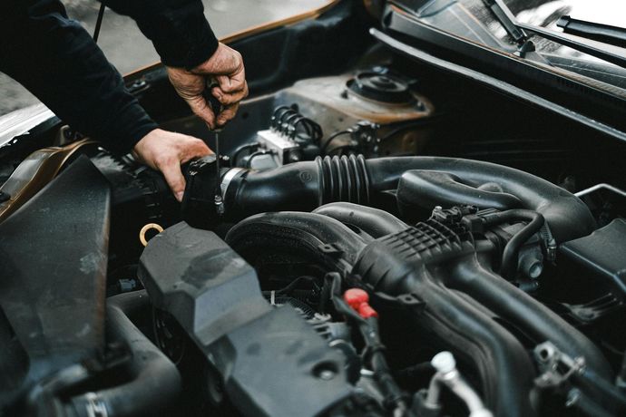 Hands working on a car engine in an open hood bay