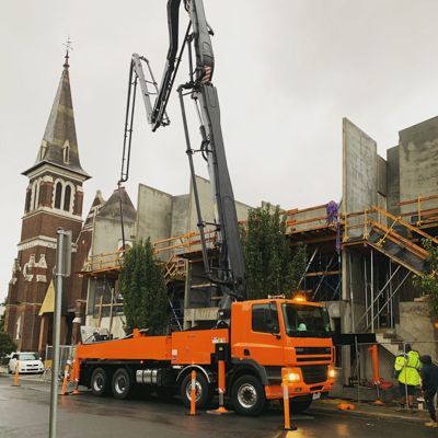 An orange truck with a crane attached to it is parked in front of a building under construction.