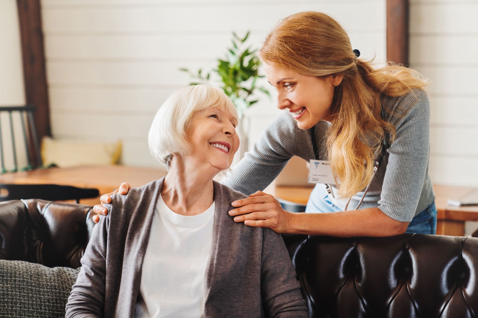 A young woman is putting her arm around an older woman sitting on a couch.