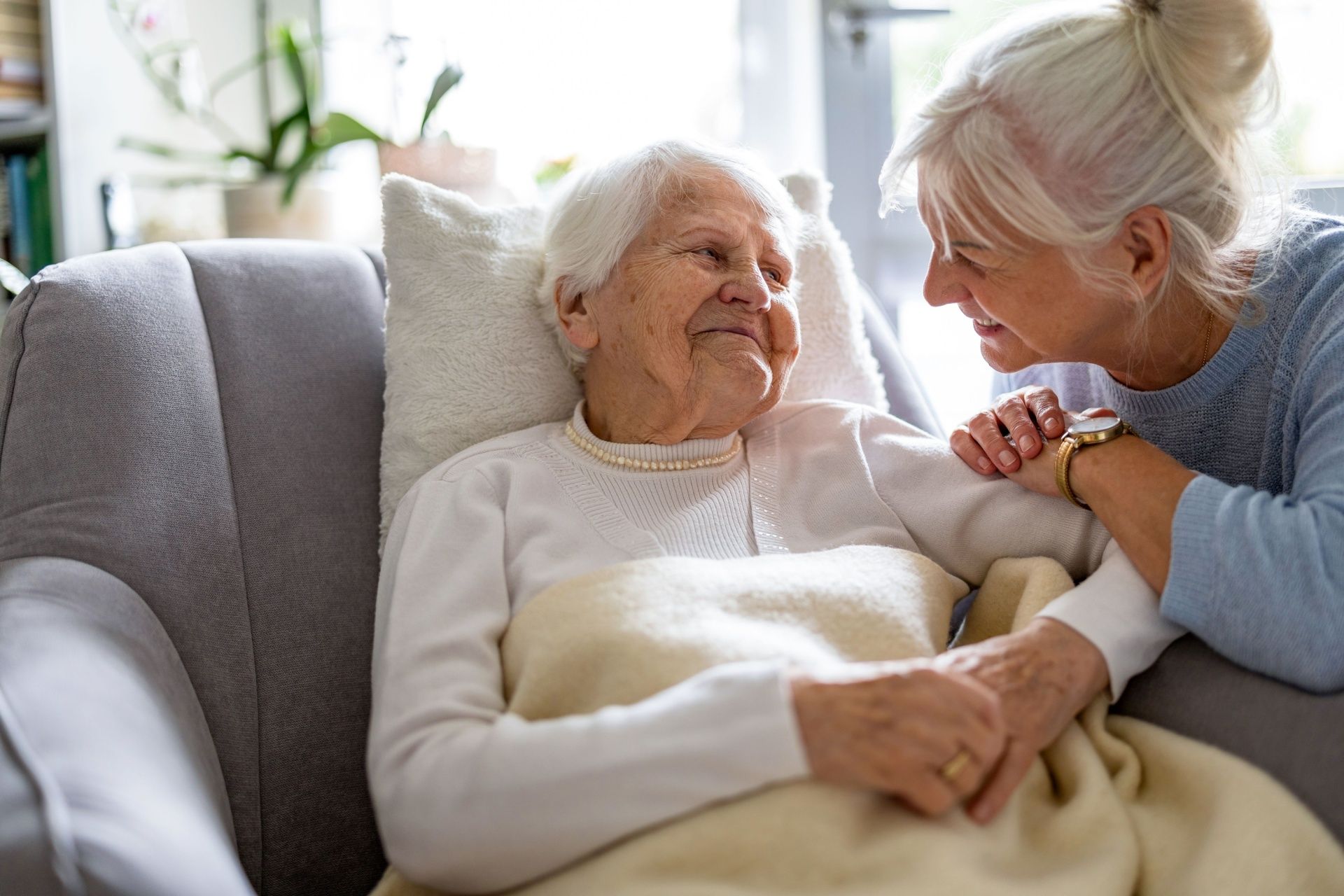 A woman is sitting next to an elderly woman in a chair.