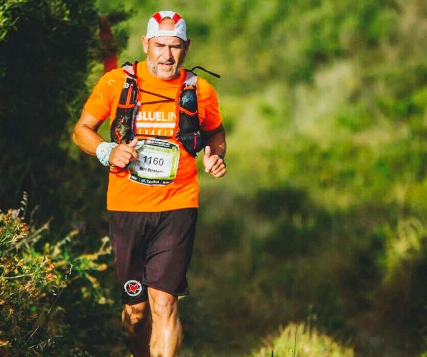 Un hombre con una camisa naranja corre por un bosque.