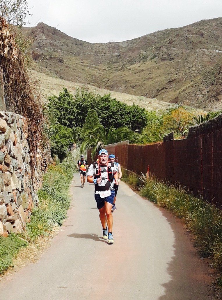 Un grupo de personas corre por una carretera con montañas al fondo.