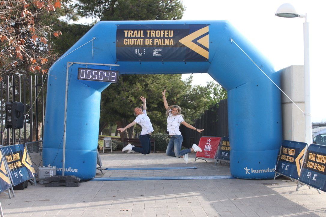 Un arco inflable azul con un cartel. Dos mujeres saltando en el centro