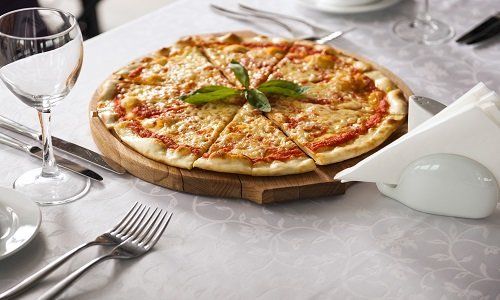 Pizza su un tagliere al centro di un tavolo apparecchiato