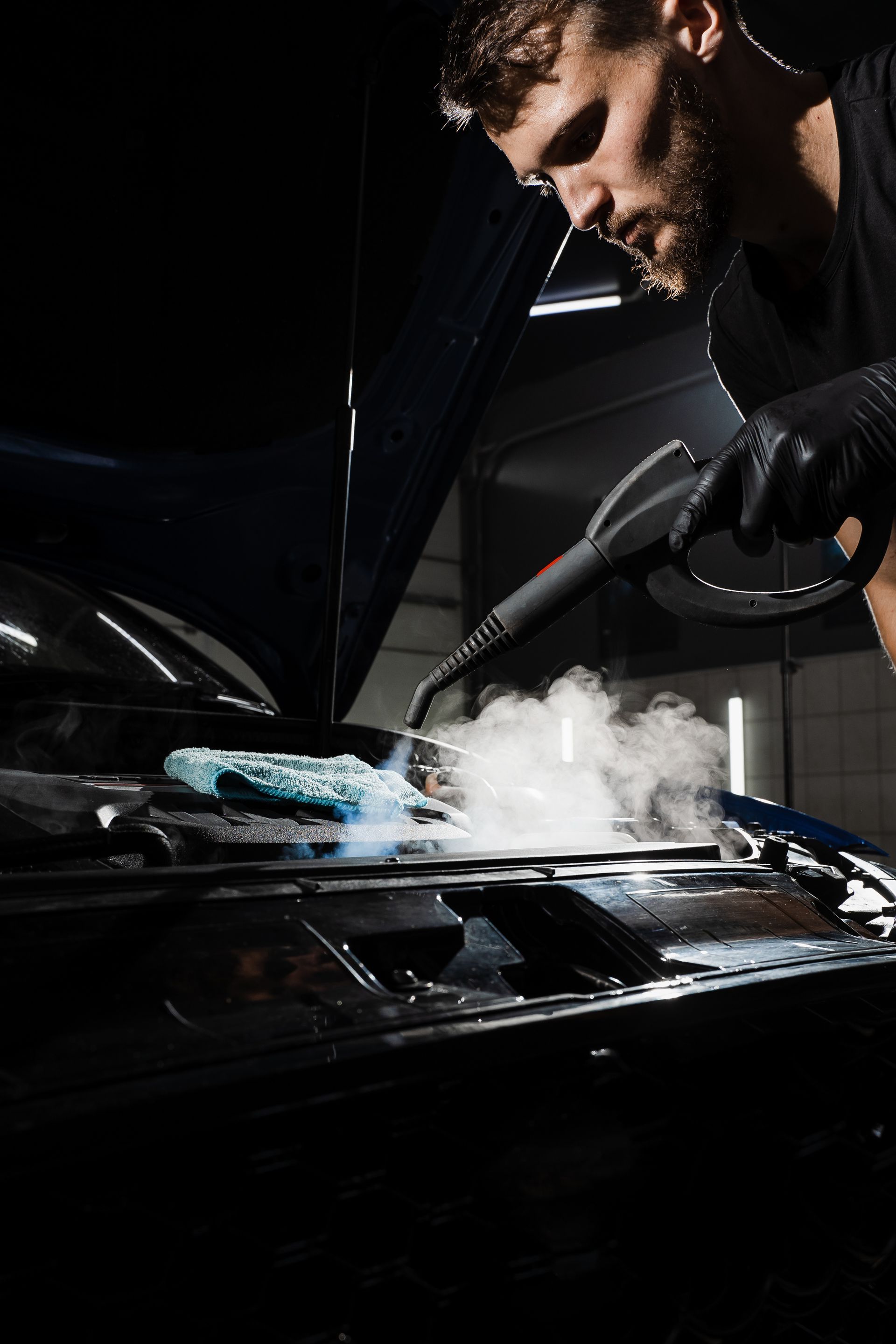 A man is cleaning the hood of a car with a steam cleaner.