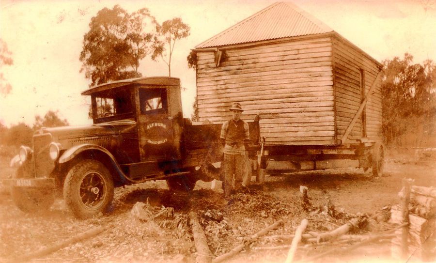 A black and white photo of a truck carrying a house.