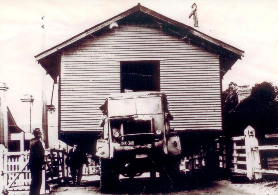 A black and white photo of a house being moved by a truck
