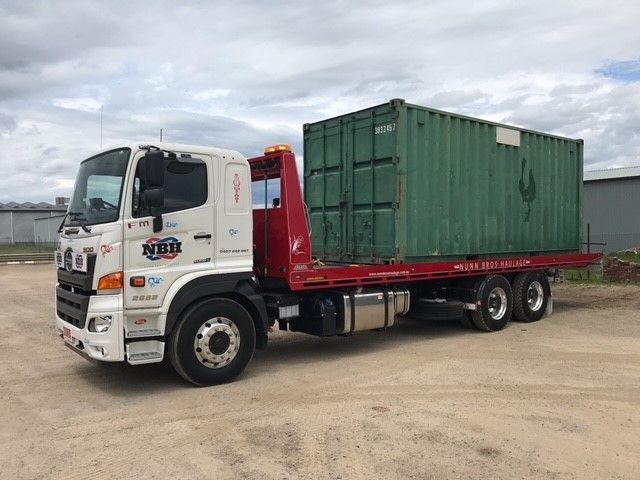 A tow truck with a green container on the back is parked in a dirt lot.