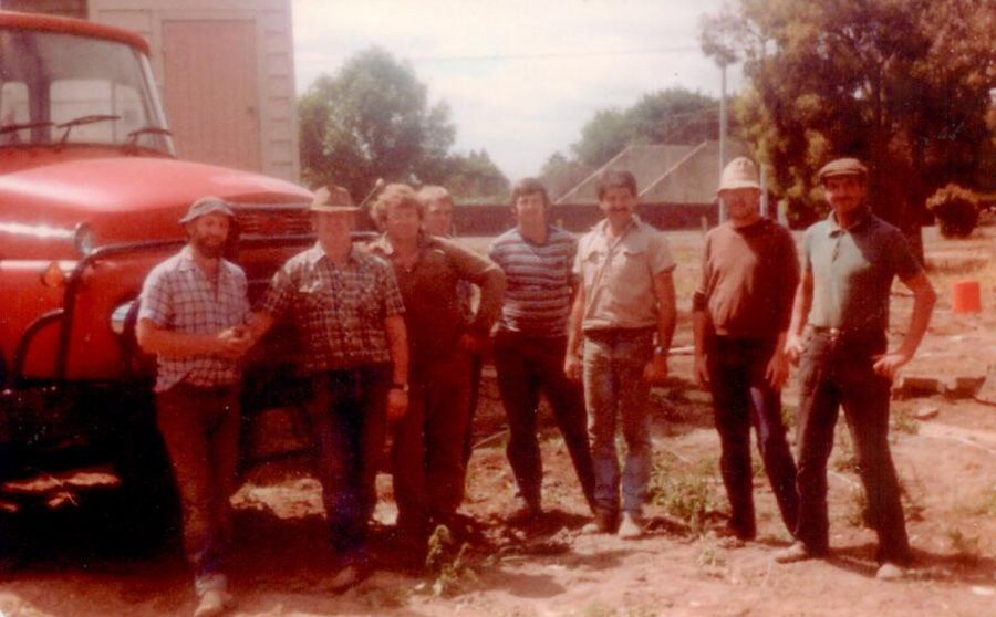 A group of men are standing in front of a red truck.