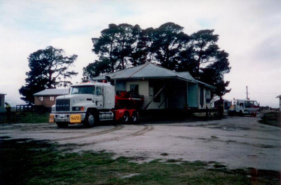 A large truck is parked in front of a house that is being moved