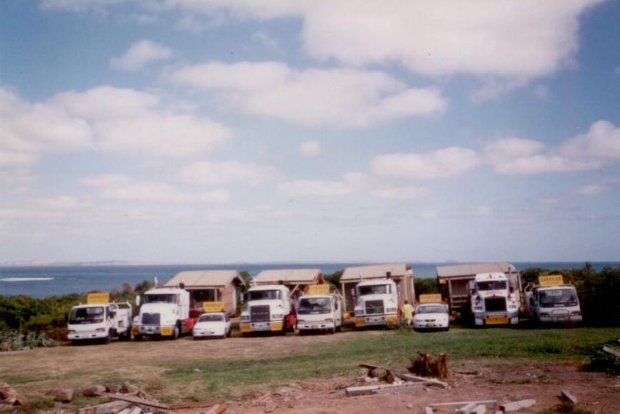 A row of trucks are parked in a field near the ocean