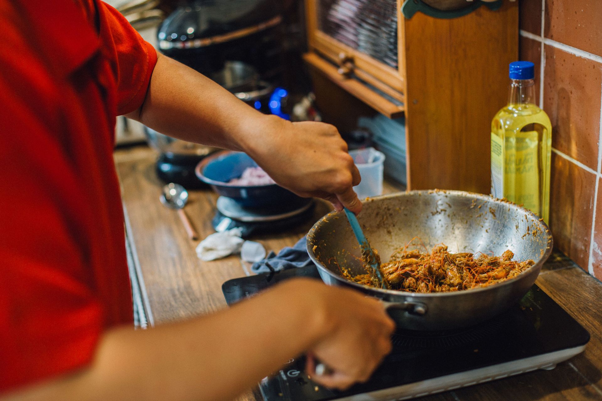 Person stirring food in a wok on a stovetop, with oil bottles and dishes nearby.