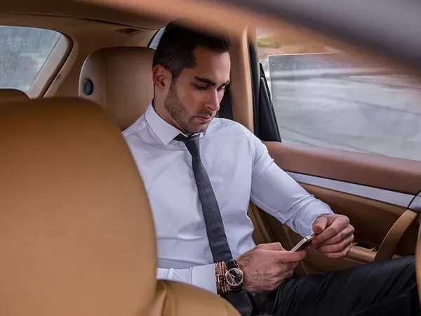 Man in white shirt and tie looking at phone in car.