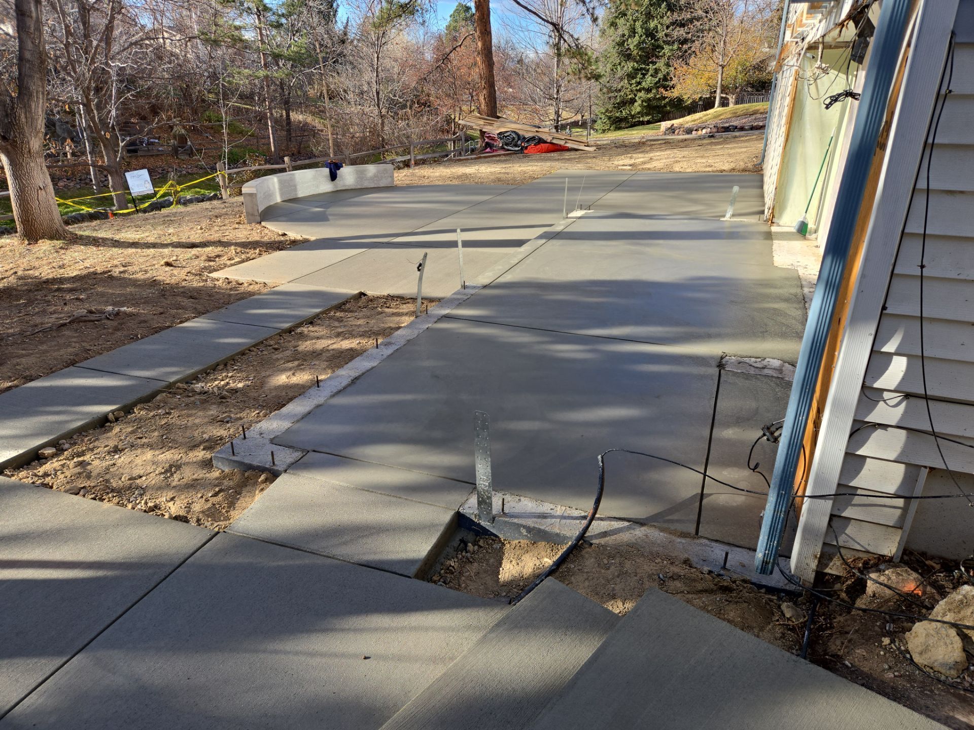 Freshly poured concrete driveway and sidewalk, next to a beige house, under construction.