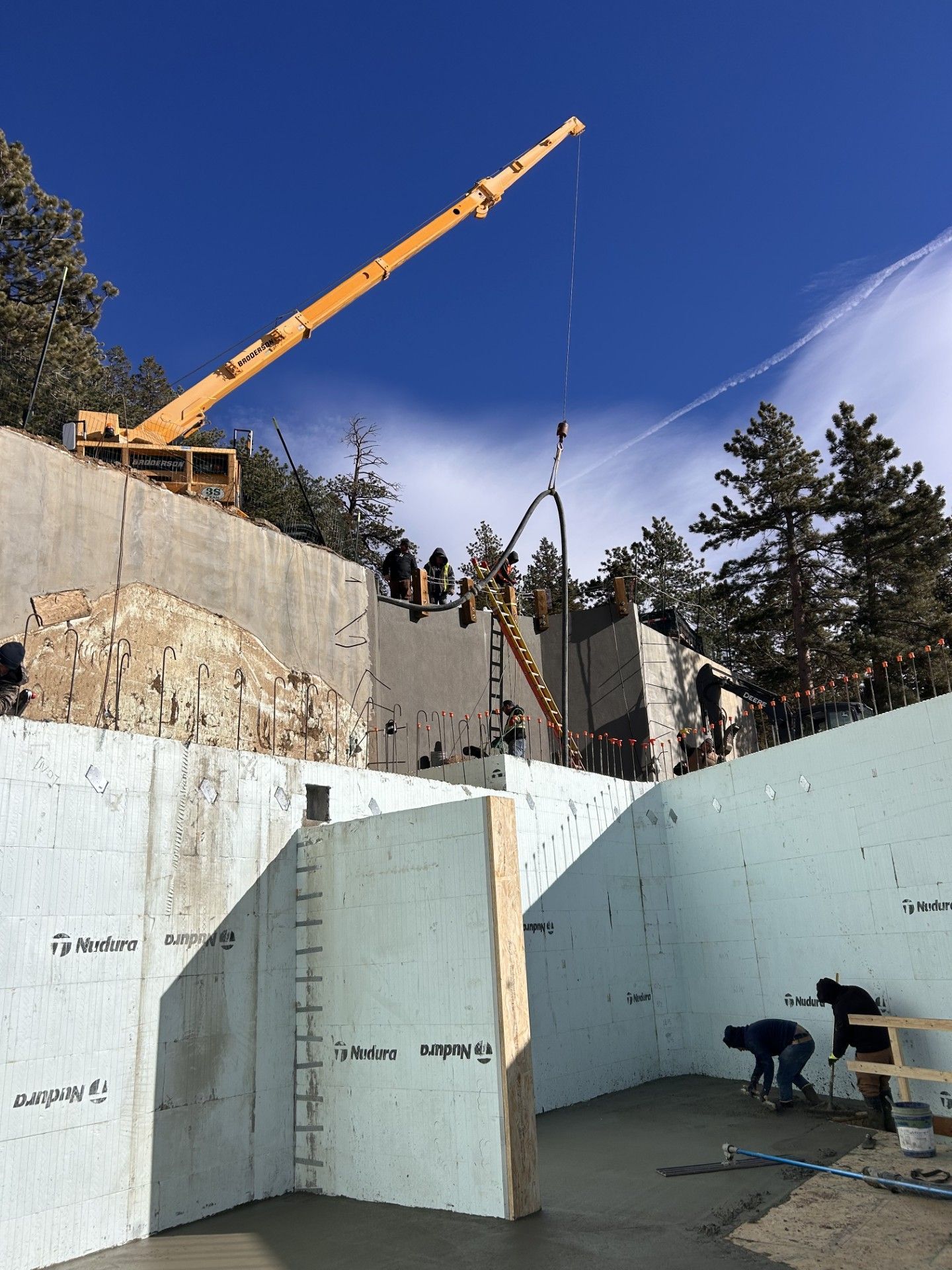 Construction site with a crane pouring concrete into insulated concrete forms. Blue sky, workers.