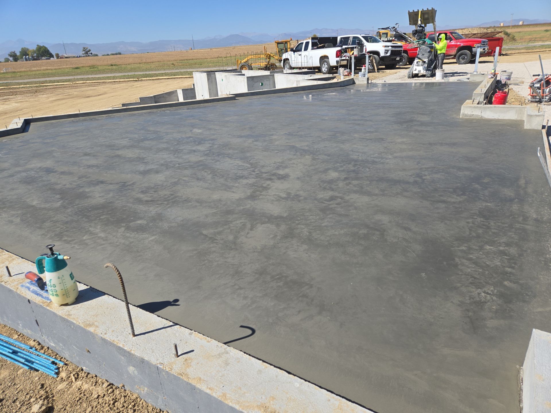 Freshly poured concrete slab at a construction site, with workers and vehicles visible in the background.