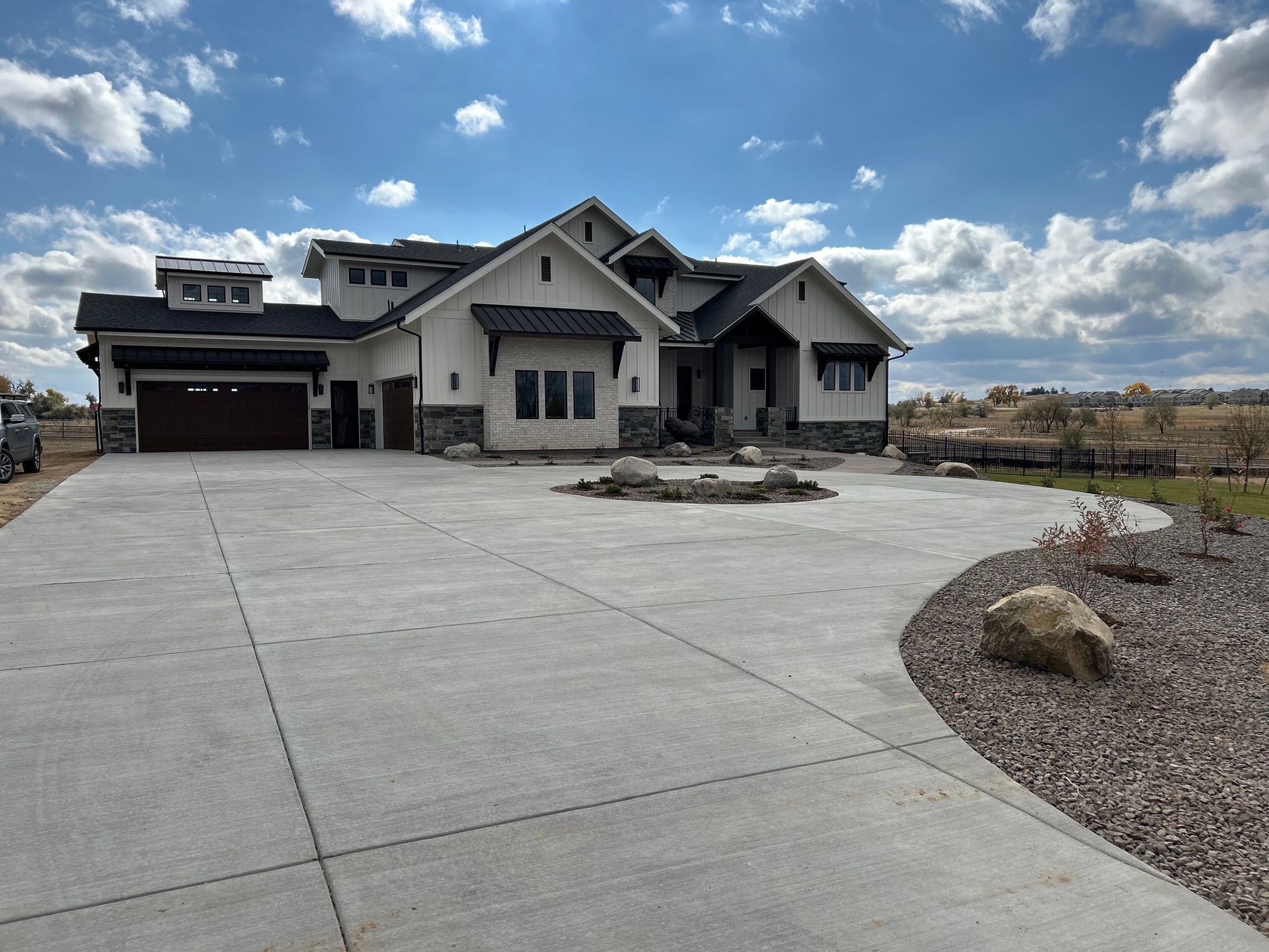 Large, modern, white house with dark trim, long concrete driveway, and a blue sky.