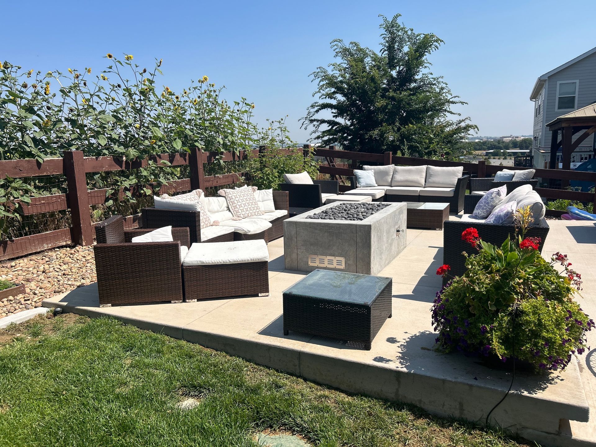 Patio with seating around a concrete fire pit. Outdoor space with green grass and a wooden fence.