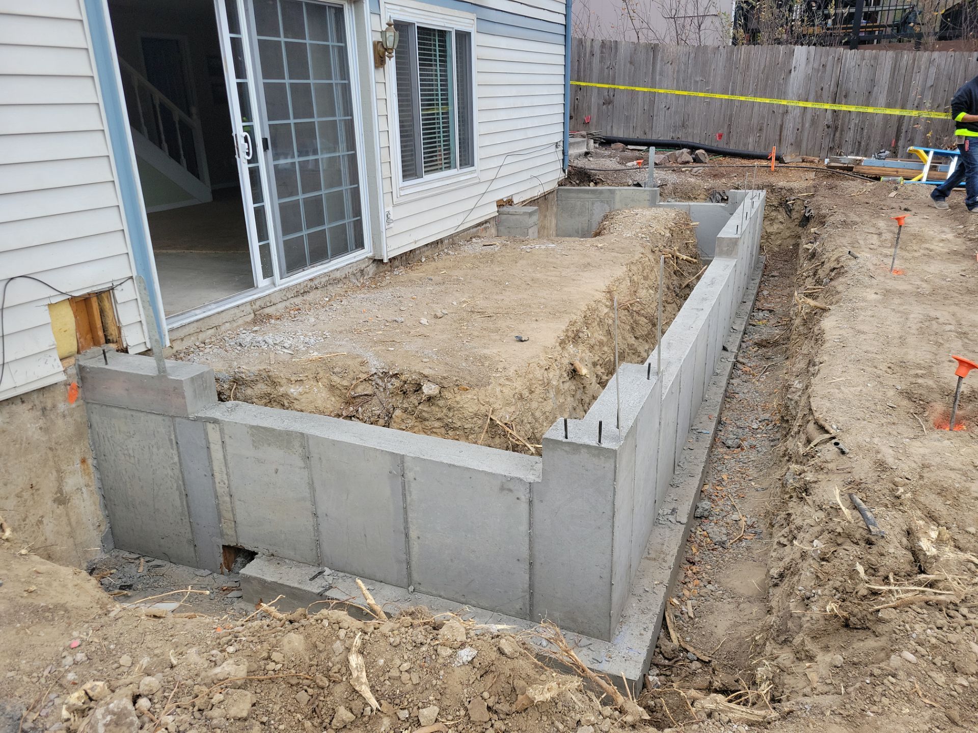 Concrete foundation construction next to a house with a sliding glass door. Ground is dirt.