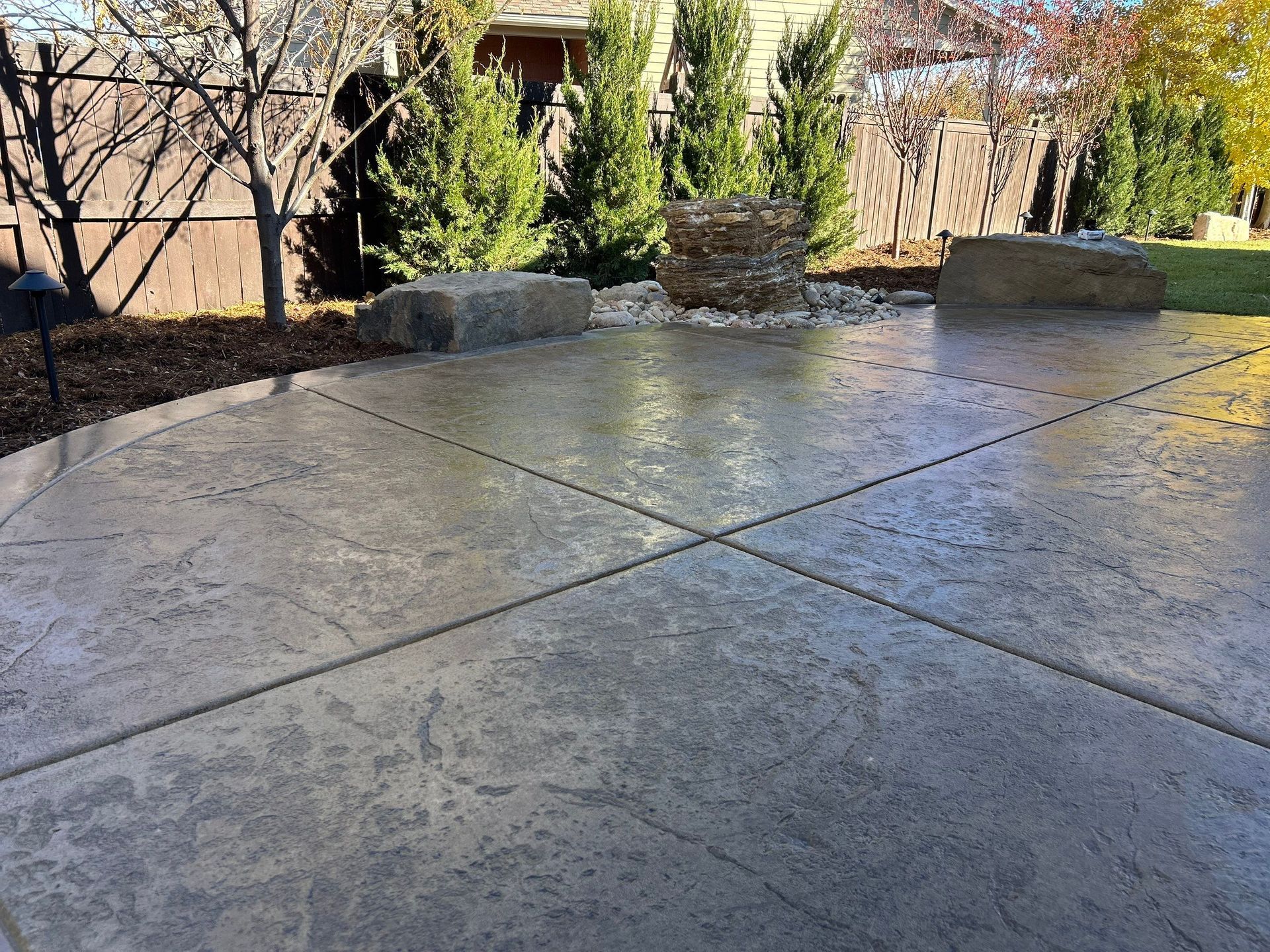 Concrete patio with rock accents, trees, and brown fence in background.
