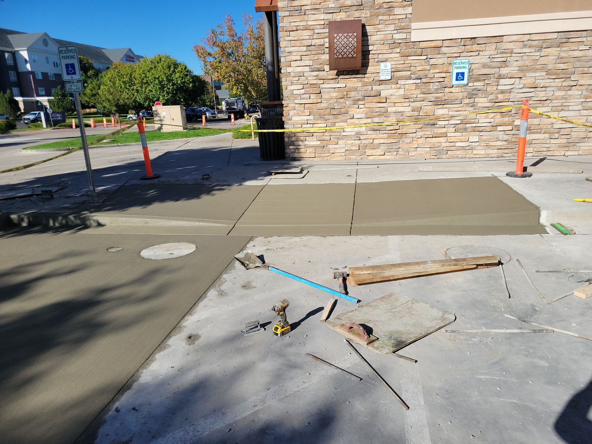 Sidewalk construction near a brick building. Concrete wet and in place; tools and barriers present.