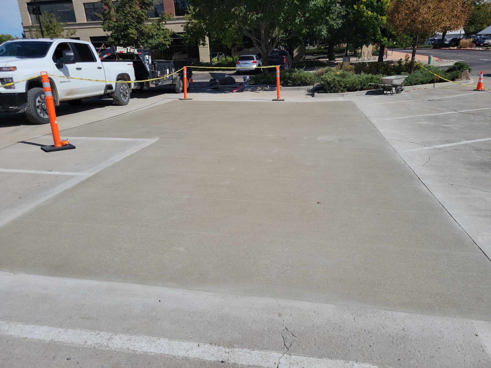 Freshly poured concrete in a parking space, surrounded by construction cones and a truck.