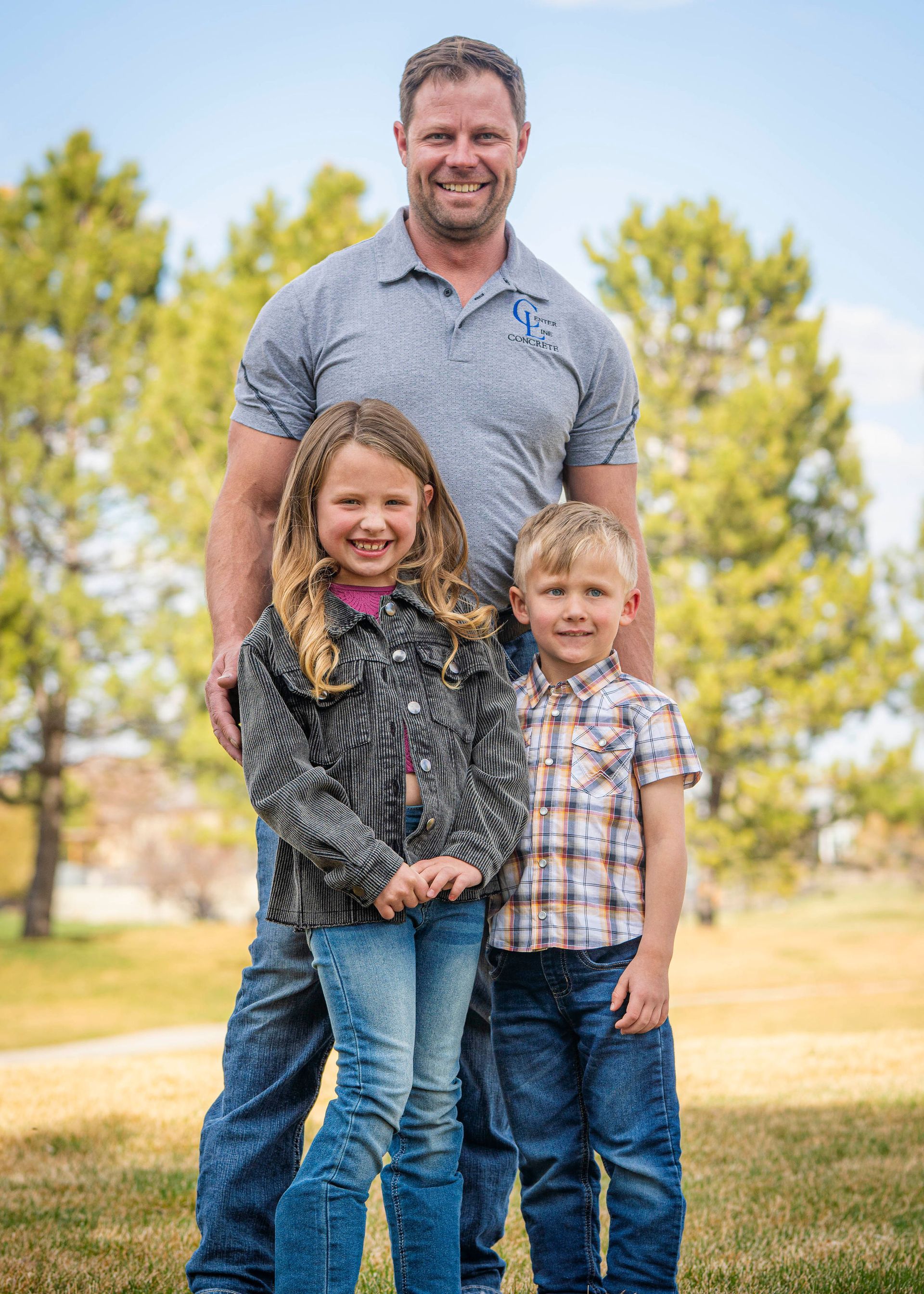 Man standing with two smiling children in a field of grass.