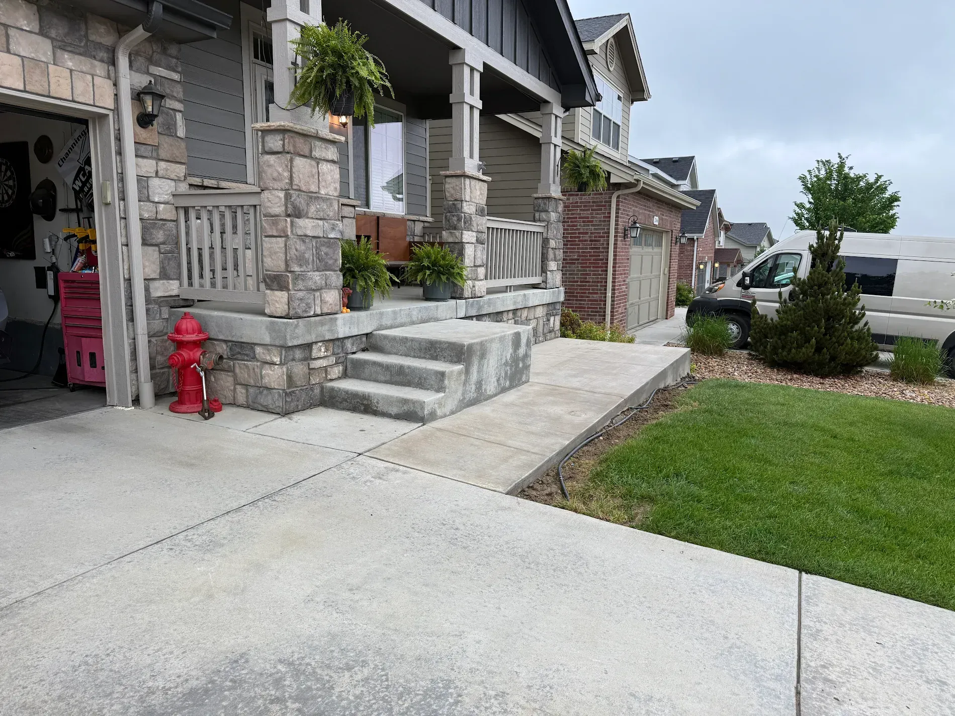 Concrete pathway leads to a house with stone steps, a porch, and green lawn. Fire hydrant and garage visible.