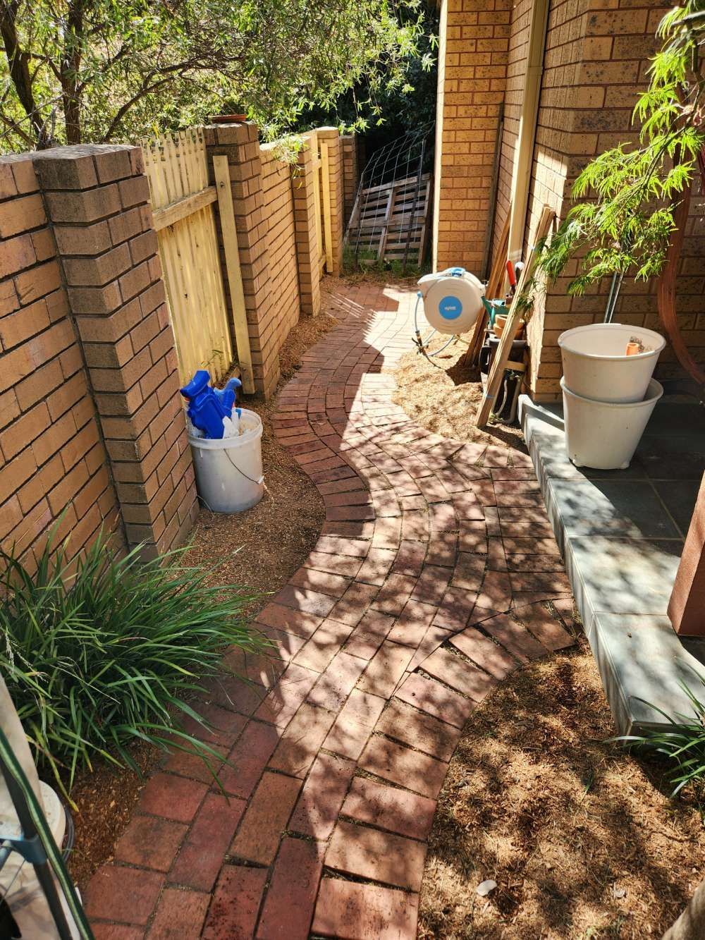 After A Brick Walkway Leading To A Fence With Buckets And Shovels — Canberra Home and Garden Maintenance in Tuggeranong ACT