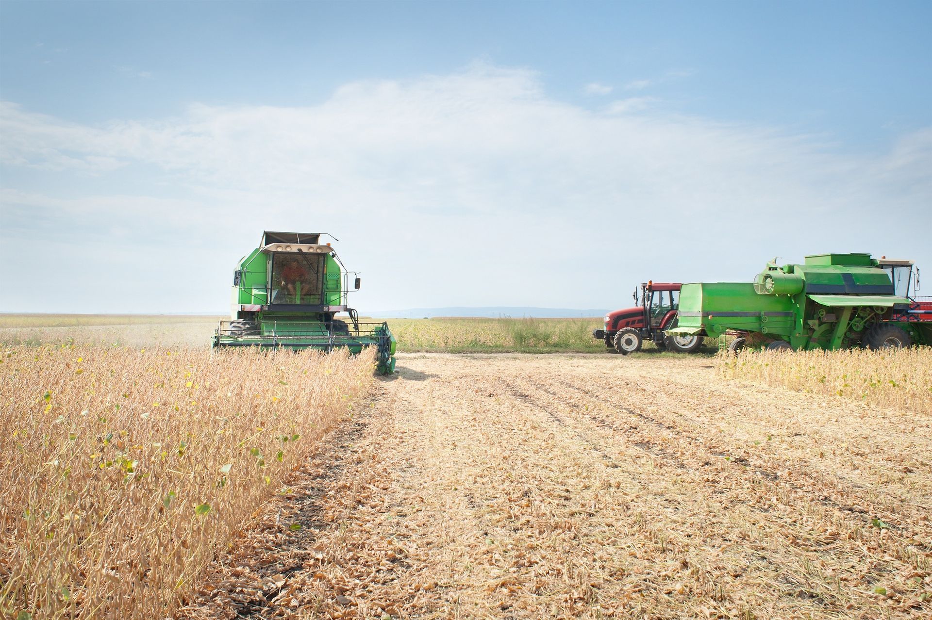 A green combine harvester and a red tractor are in a field |  HHO Carbon Clean Systems - North Atlanta