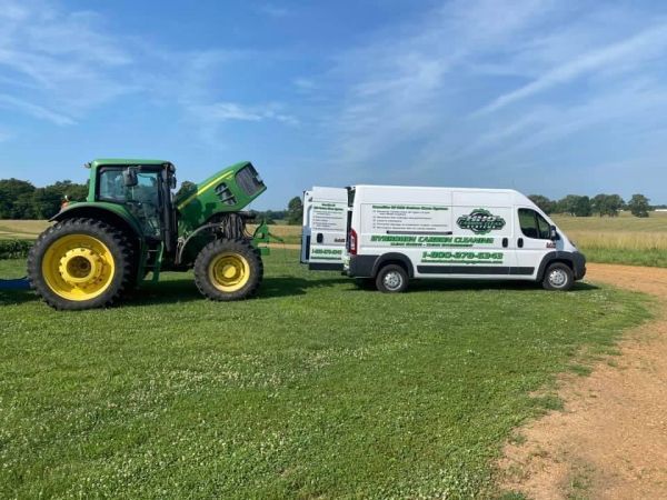 A tractor is being towed by a white van in a field | HHO Carbon Clean Systems - North Atlanta