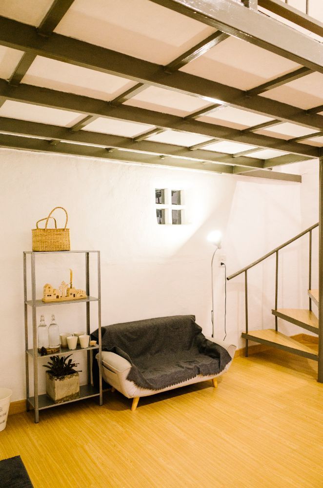 Cozy living space with a sofa, shelving unit, and a loft bed accessed by stairs.