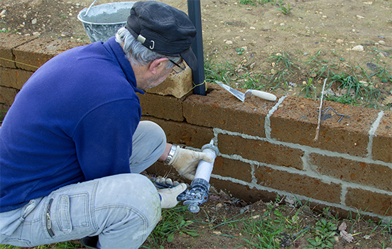 Green, rusty metal support on a concrete block wall, holding a horizontal pipe.