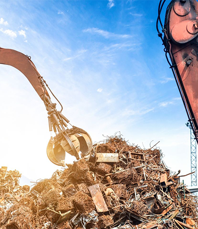 Claw of a machine lifting scrap metal from a large pile against a blue sky.