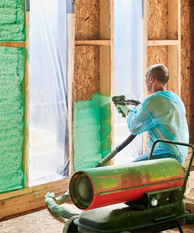 Man spraying green foam insulation into a wooden wall. A large machine sits nearby.