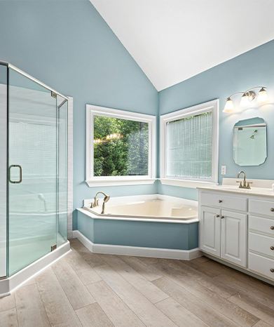 Bathroom with a corner bathtub, shower, white vanity, and light blue walls.