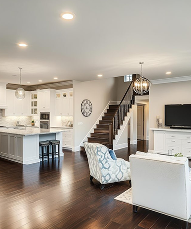 Open-concept living space with kitchen and living room. White cabinets, island, dark hardwood floors, staircase, and neutral colors.