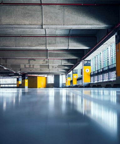 Empty, modern parking garage. Concrete ceiling and pillars. Yellow parking signs, reflective floor, bright daylight.