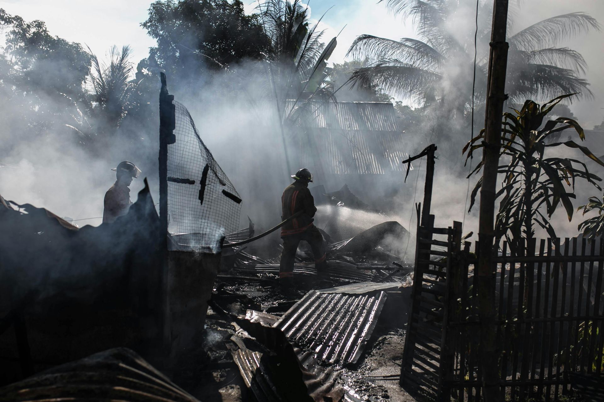 Firefighters battle a blaze at a home, spraying water amidst smoke and charred debris.