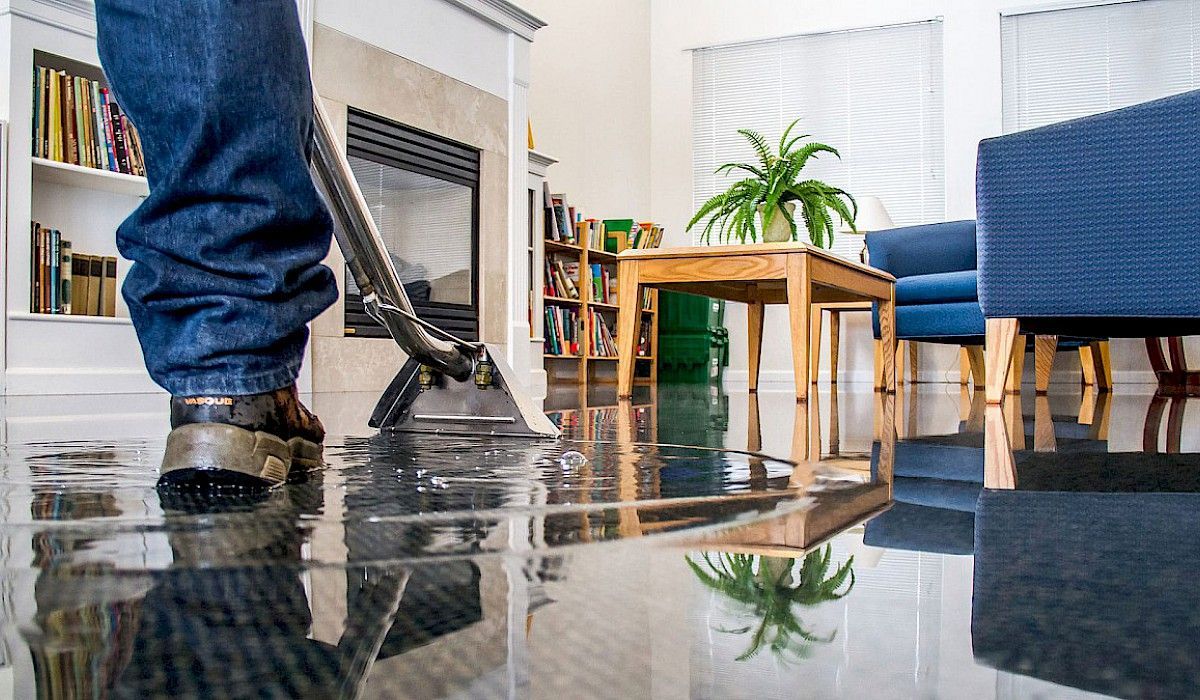 A person is vacuuming a flooded floor in a living room Water Damage Restoration in Denver