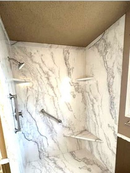 A shower with marble walls and shelves and a shower head.