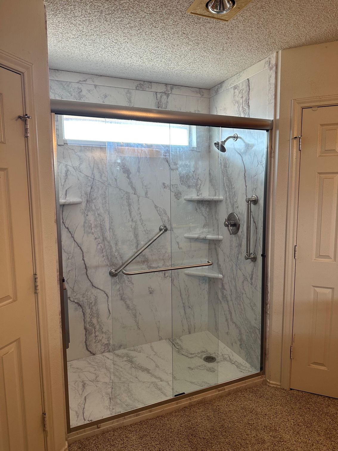 A bathroom with a walk in shower with marble walls and a sliding glass door.