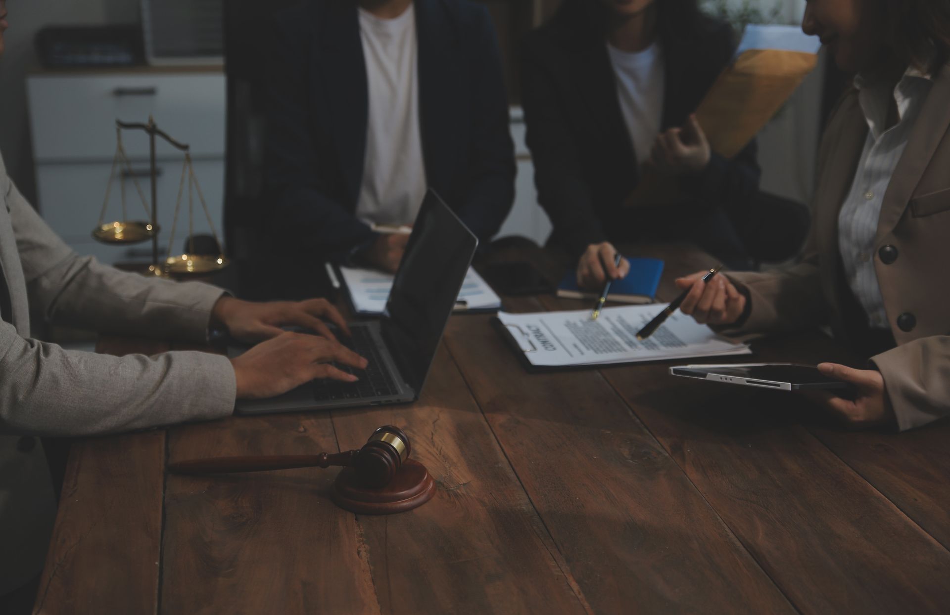 A group of people are sitting around a wooden table with laptops and papers.