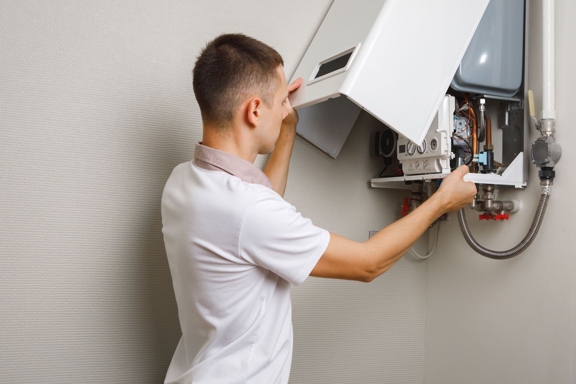 Man installing or repairing a wall-mounted heating unit, indoors.
