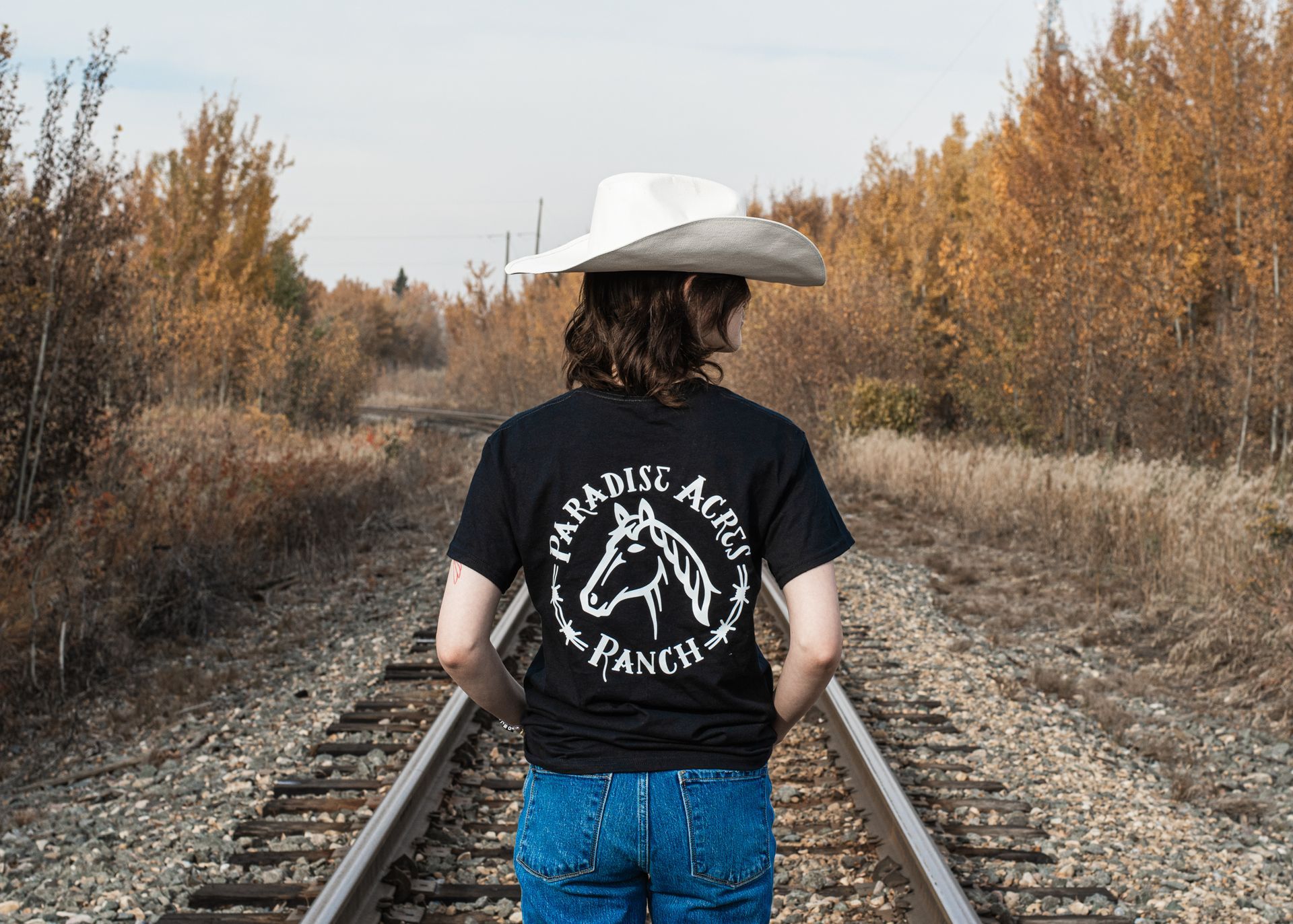 A woman wearing a cowboy hat is standing on train tracks.