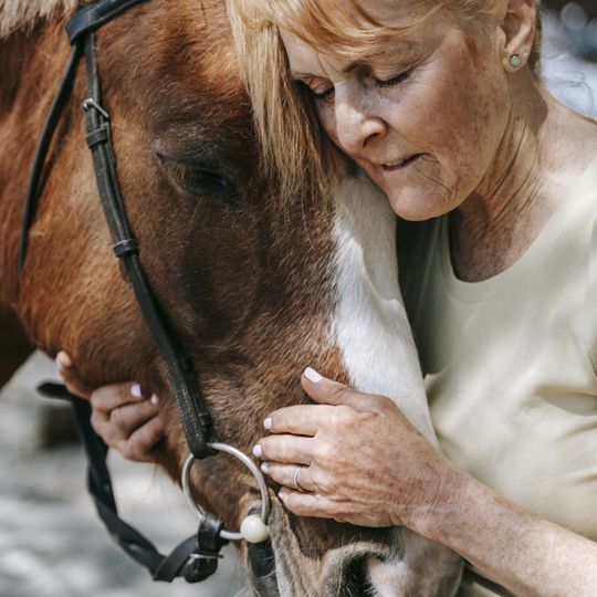 An older woman hugging the head of a horse