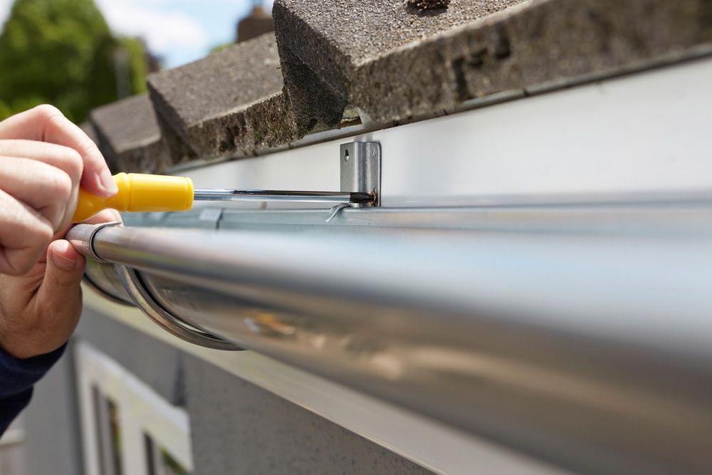 A man is installing a gutter on the side of a house.